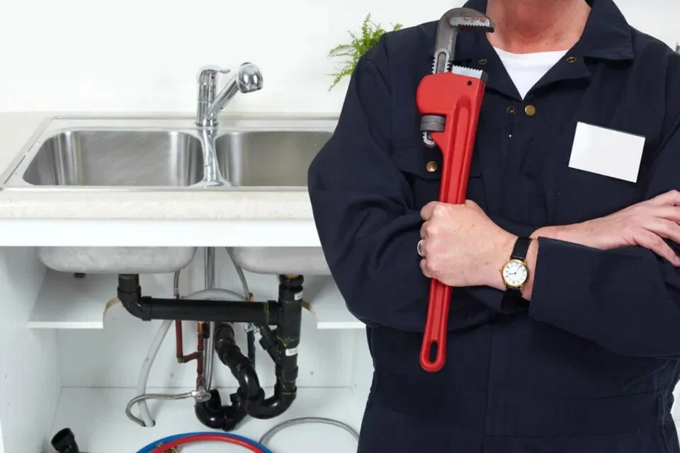 Vakman met gereedschap naast een dubbele gootsteen met zichtbare afvoerleidingen